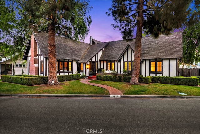 english style home with stucco siding, a front lawn, and fence