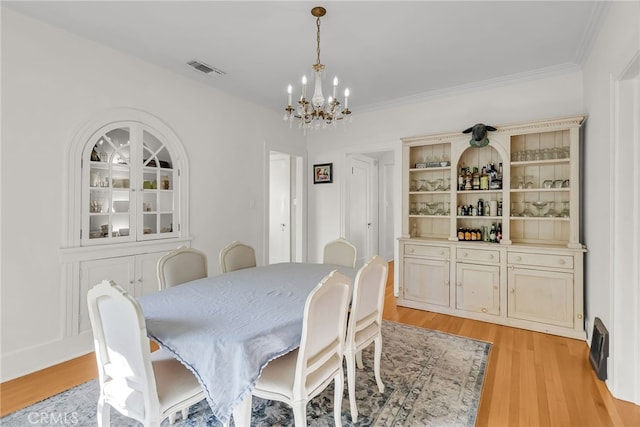 dining space with a notable chandelier, visible vents, light wood finished floors, and ornamental molding