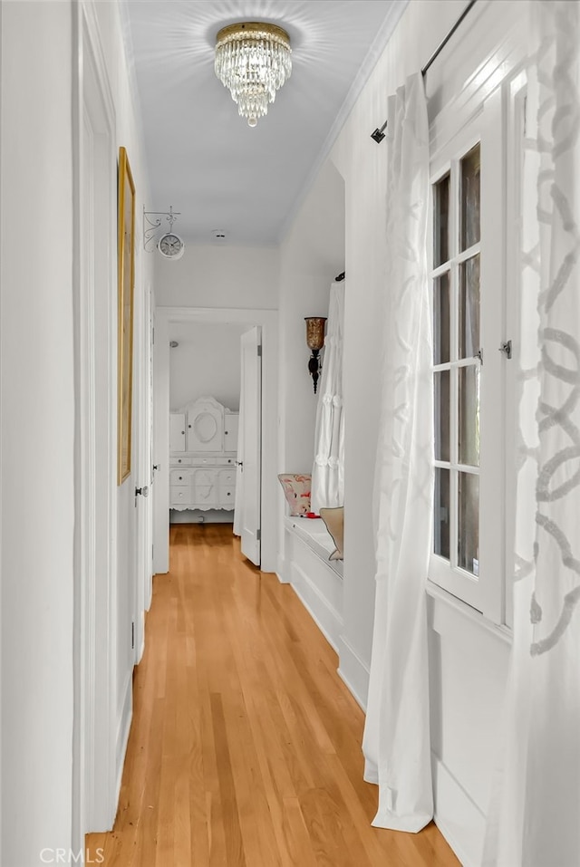 hallway with light wood-style flooring, crown molding, and an inviting chandelier