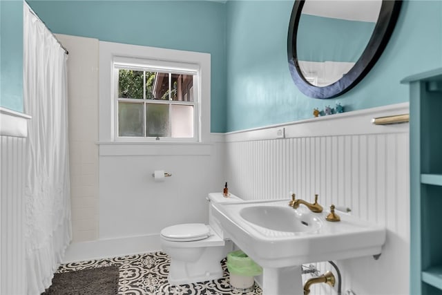 bathroom with a shower with shower curtain, tile patterned floors, toilet, and a wainscoted wall