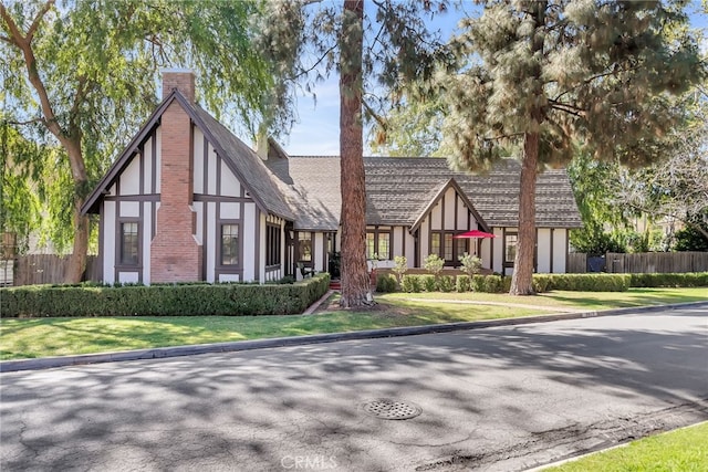 tudor-style house with fence, a chimney, and stucco siding