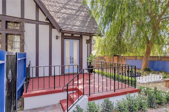 entrance to property with french doors, fence, roof with shingles, and stucco siding