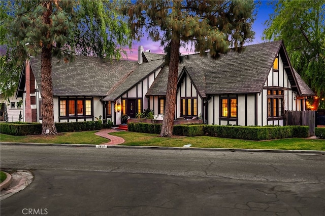 tudor home with a yard, fence, and stucco siding