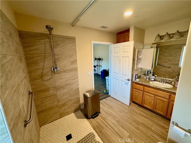 full bath with visible vents, tiled shower, vanity, and wood finished floors