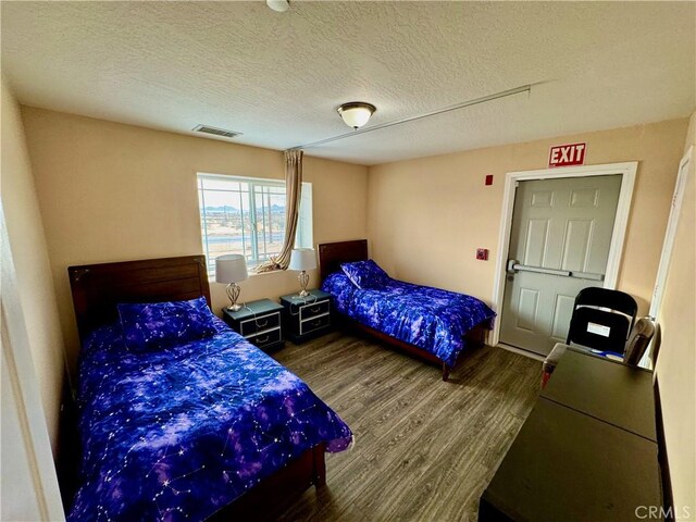 bedroom with visible vents, a textured ceiling, and wood finished floors