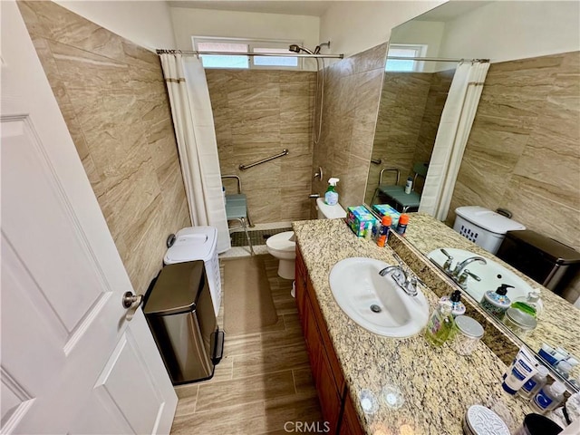 bathroom with toilet, tile walls, vanity, and a tile shower