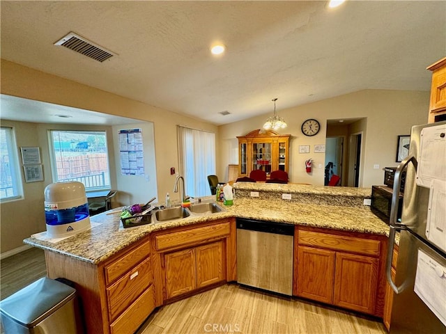 kitchen featuring visible vents, a sink, stainless steel appliances, vaulted ceiling, and brown cabinets