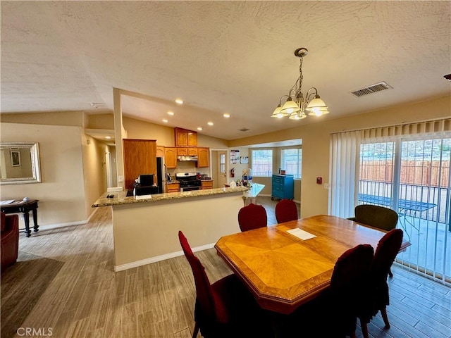 dining room with light wood-type flooring, a textured ceiling, visible vents, and vaulted ceiling