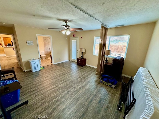 interior space with visible vents, a textured ceiling, wood finished floors, baseboards, and ceiling fan