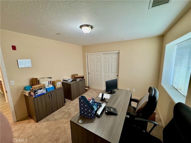 office area featuring visible vents, baseboards, light colored carpet, and a textured ceiling