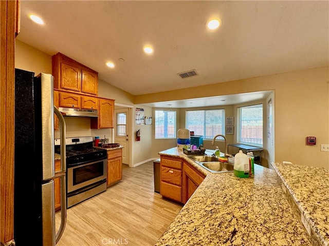 kitchen featuring visible vents, a sink, under cabinet range hood, stainless steel appliances, and brown cabinetry