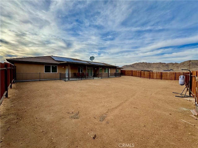 rear view of house featuring a fenced backyard, stucco siding, a patio area, a mountain view, and roof mounted solar panels