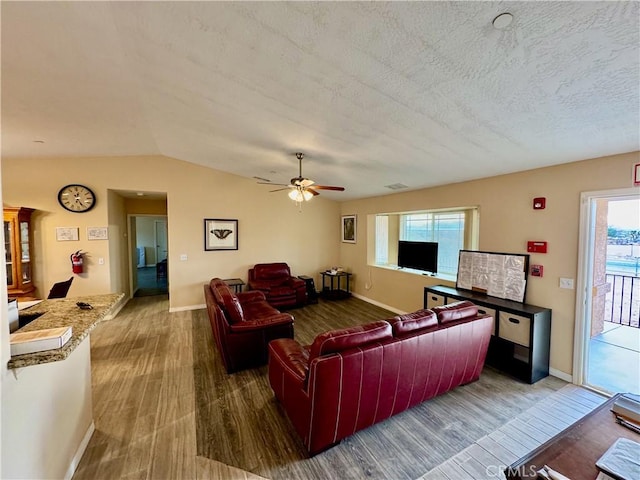 living area with vaulted ceiling, a textured ceiling, visible vents, and wood finished floors