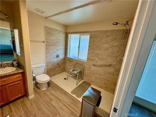 full bathroom featuring visible vents, toilet, tiled shower, wood finished floors, and vanity