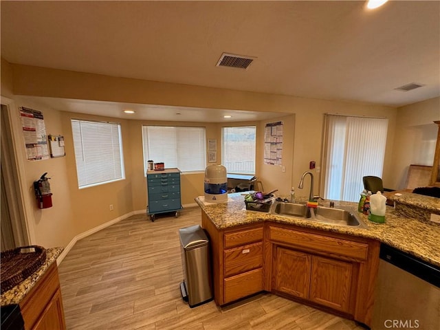 kitchen with brown cabinetry, visible vents, a sink, light wood-style floors, and stainless steel dishwasher