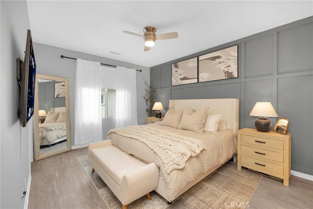 bedroom with light wood finished floors, a ceiling fan, and a decorative wall