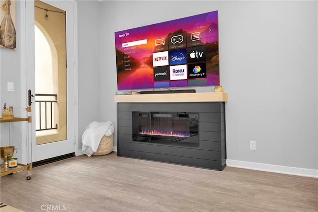 living area featuring baseboards, wood finished floors, arched walkways, and a glass covered fireplace