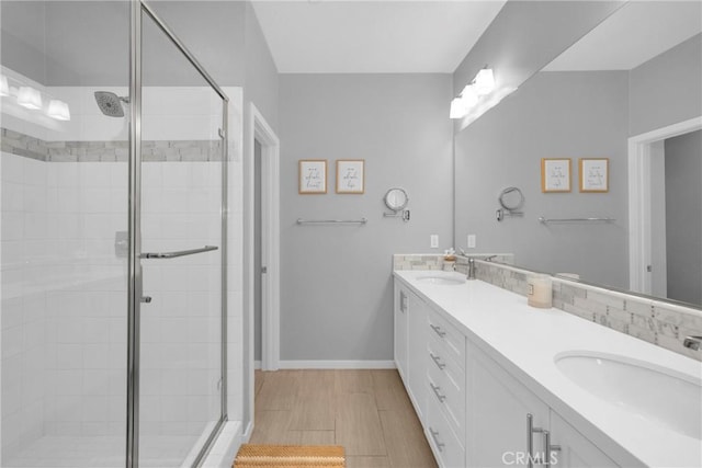 bathroom featuring a sink, baseboards, a stall shower, and double vanity