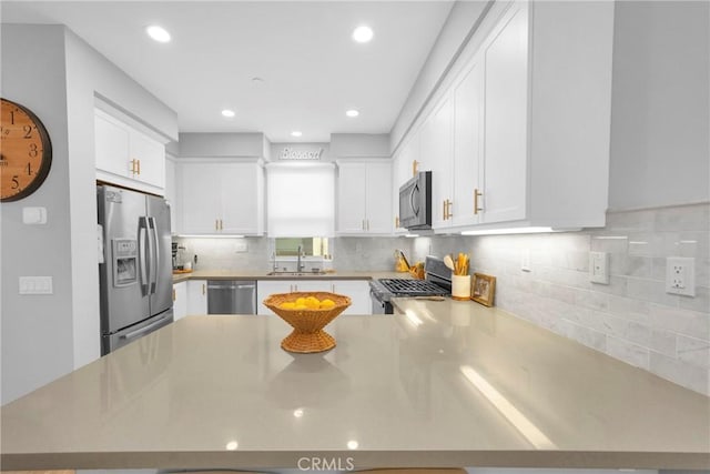 kitchen with white cabinetry, a peninsula, stainless steel appliances, and a sink