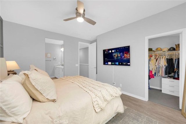 bedroom featuring wood finished floors, baseboards, ensuite bath, a spacious closet, and a closet