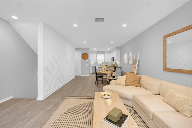 living area with recessed lighting, visible vents, light wood finished floors, and baseboards