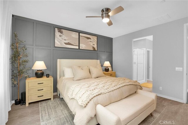 bedroom featuring visible vents, a ceiling fan, wood finished floors, a decorative wall, and baseboards