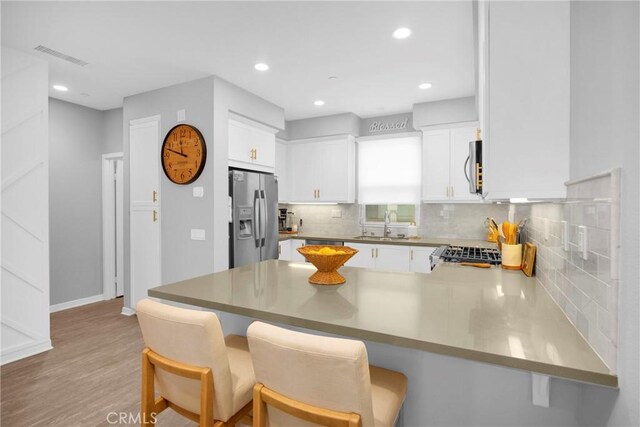 kitchen with visible vents, appliances with stainless steel finishes, a peninsula, white cabinets, and a sink