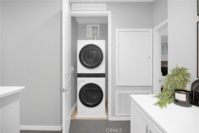 washroom featuring visible vents, baseboards, stacked washer and clothes dryer, and laundry area