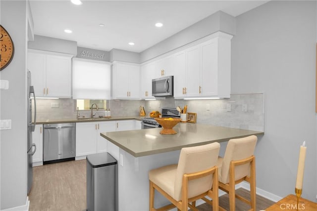 kitchen featuring a sink, stainless steel appliances, a peninsula, and white cabinets