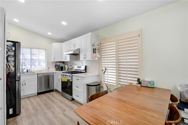 kitchen featuring under cabinet range hood, light countertops, light wood-type flooring, vaulted ceiling, and appliances with stainless steel finishes