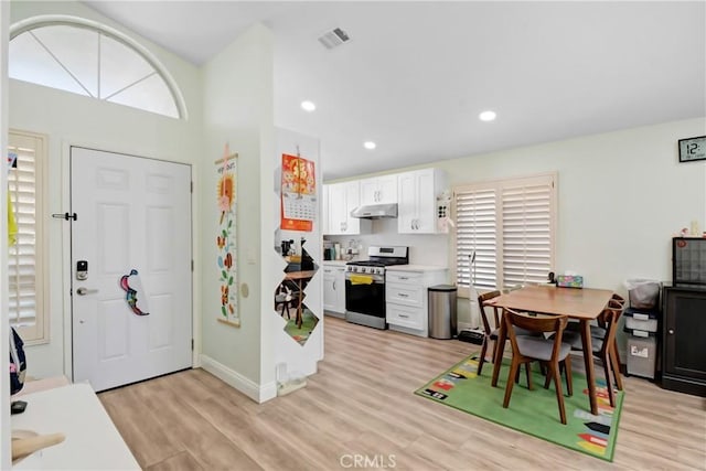 kitchen with under cabinet range hood, stainless steel range with gas stovetop, recessed lighting, light wood-style floors, and white cabinetry