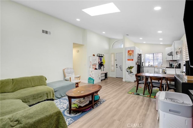 living room featuring vaulted ceiling with skylight, recessed lighting, light wood-style flooring, and visible vents