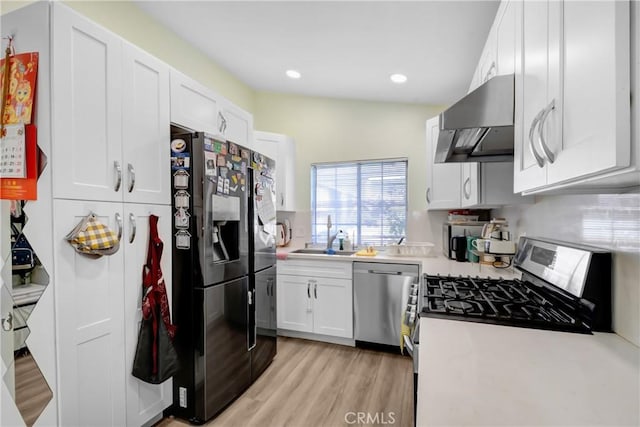 kitchen featuring a sink, stainless steel appliances, wall chimney exhaust hood, white cabinets, and light countertops