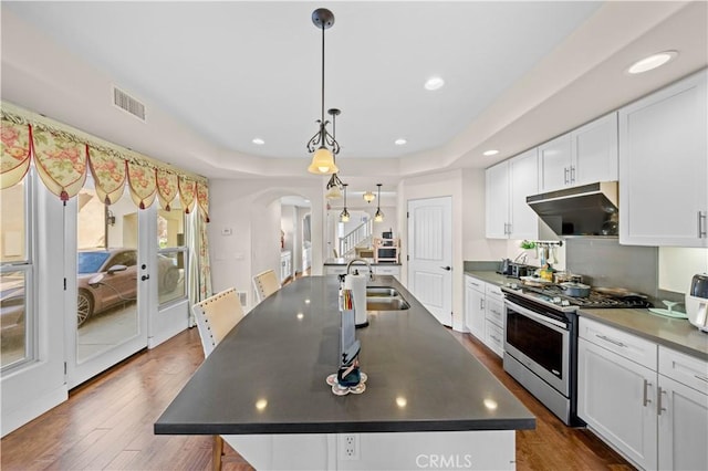 kitchen with under cabinet range hood, a sink, dark countertops, arched walkways, and gas range