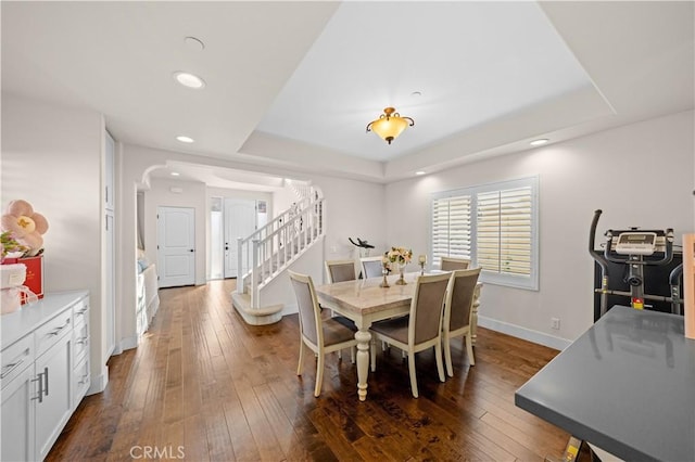 dining room featuring stairway, dark wood-style floors, baseboards, recessed lighting, and a raised ceiling