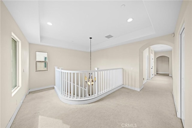 corridor with arched walkways, carpet flooring, a raised ceiling, and baseboards