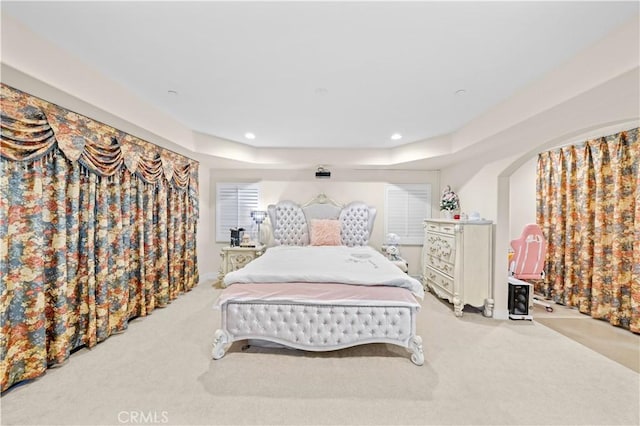 carpeted bedroom with recessed lighting, a raised ceiling, and arched walkways