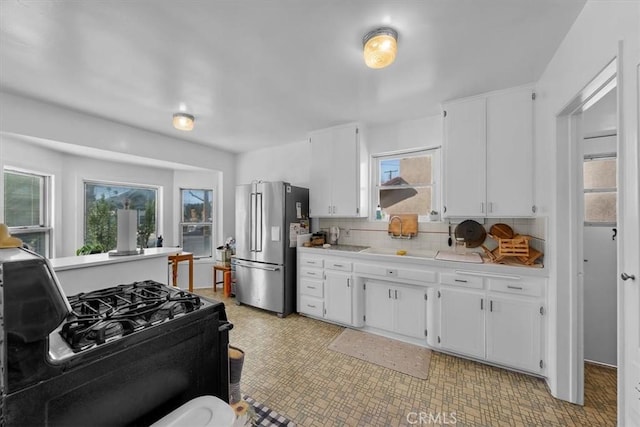 kitchen featuring decorative backsplash, white cabinetry, black range with gas stovetop, and freestanding refrigerator