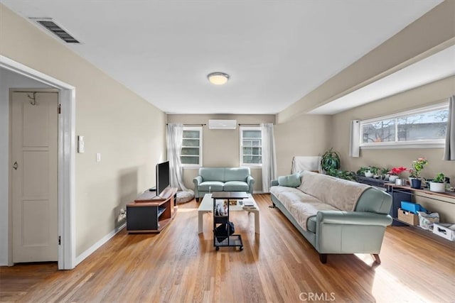 living area with visible vents, baseboards, a wall unit AC, and wood finished floors