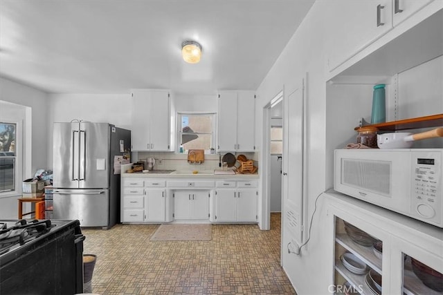 kitchen with white microwave, freestanding refrigerator, light countertops, white cabinets, and tasteful backsplash