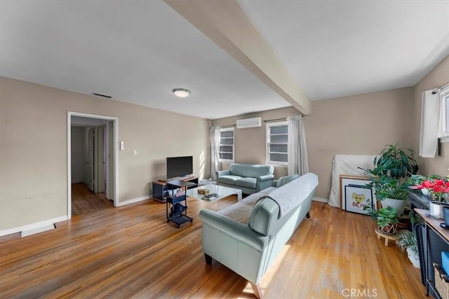 living area featuring visible vents, beam ceiling, an AC wall unit, wood finished floors, and baseboards