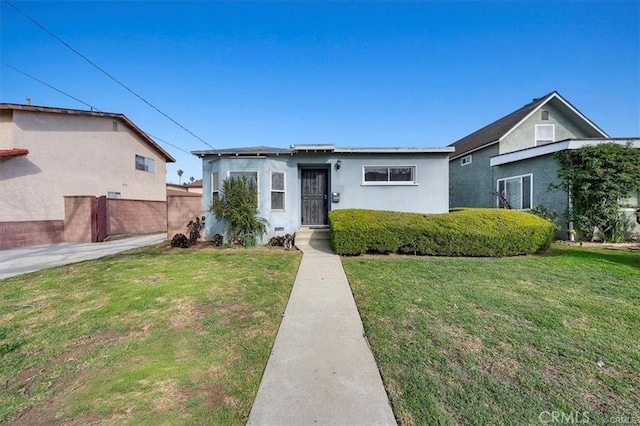 view of front facade featuring stucco siding, a front yard, and fence