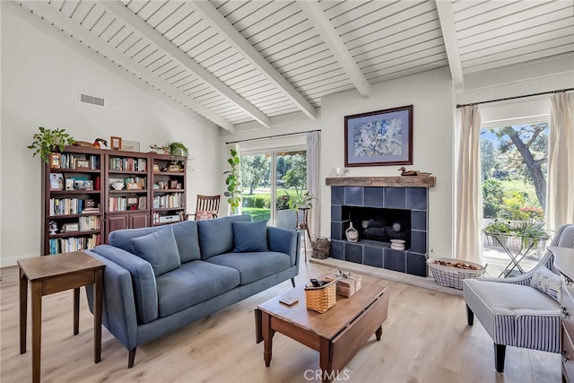 living room with a tiled fireplace, light wood-style flooring, vaulted ceiling with beams, and visible vents