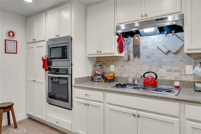 kitchen with under cabinet range hood, light countertops, decorative backsplash, appliances with stainless steel finishes, and white cabinets