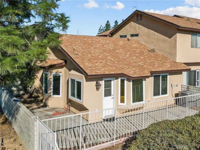 back of property featuring stucco siding, central AC unit, a fenced backyard, and a shingled roof