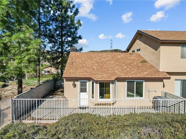 rear view of house featuring a shingled roof, fence private yard, central AC, and stucco siding