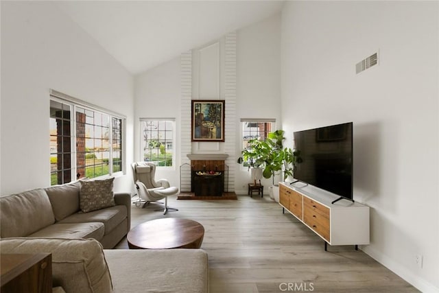 living area featuring visible vents, baseboards, light wood-style flooring, a fireplace, and high vaulted ceiling