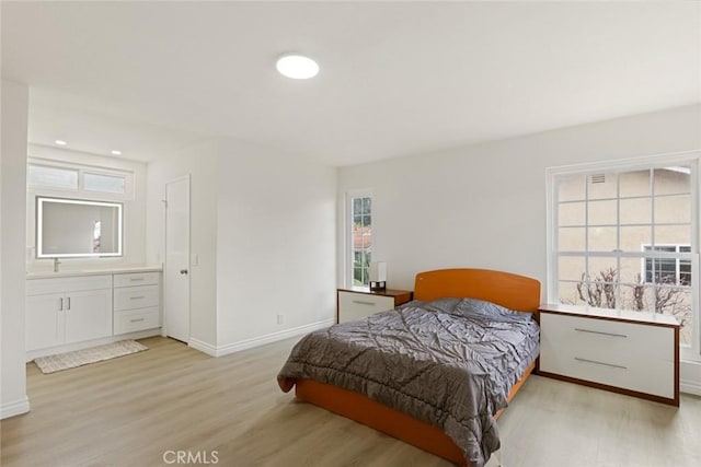 bedroom with baseboards, light wood-style flooring, and ensuite bathroom