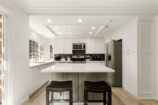 kitchen featuring light wood-style flooring, a sink, a kitchen breakfast bar, white cabinetry, and appliances with stainless steel finishes