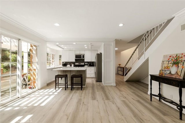 kitchen featuring a kitchen island, a breakfast bar area, light wood-style floors, white cabinets, and stainless steel appliances